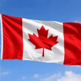 Канадско знаме с червен кленов лист, развято на фона на синьо небе