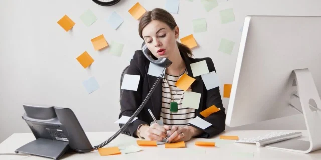 Човек говори по телефона и работи на лаптоп сред документи